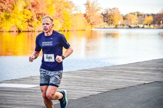 Josh Born running a race on a lakeside path in autumn, wearing a blue running top.
